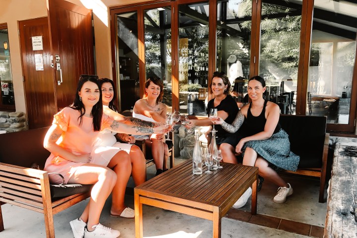 Five women sitting on patio furniture toasting with wine glasses outside a Marlborough Winery.