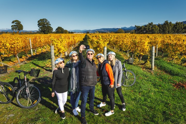 Group of people taking a selfie in a Marlborough vineyard, wearing helmets with bicycles nearby.