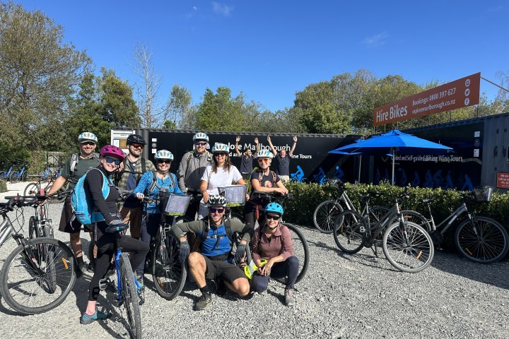 Group of cyclists with helmets posing outside a Bike Hire Marlborough on a sunny day.