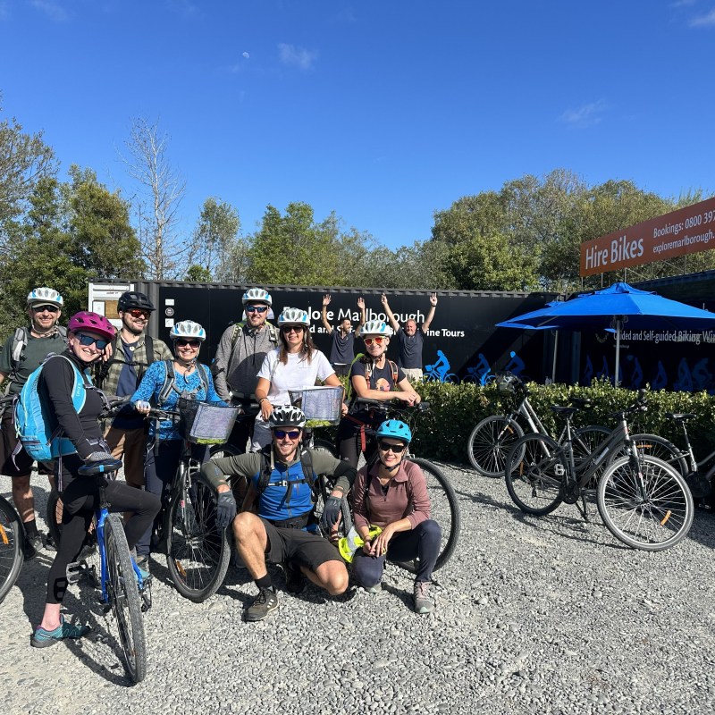 Group of cyclists with helmets posing outside a Bike Hire Marlborough on a sunny day.