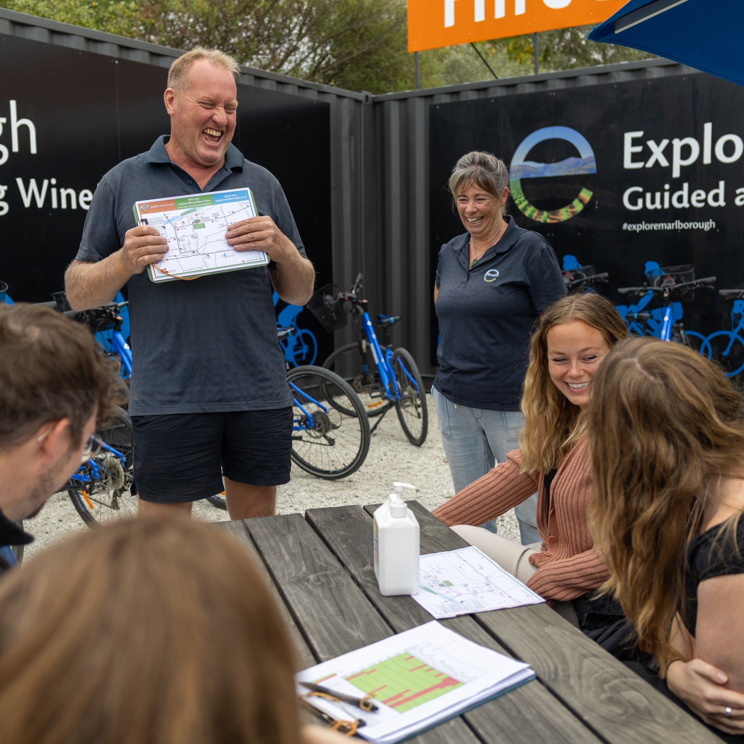 Group gathered outdoors around a map, discussing biking tours with blue bicycles in background.